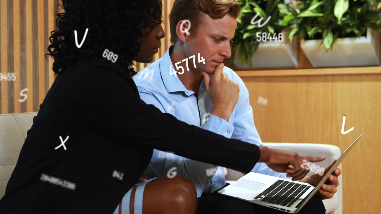 Woman reaching across laptop and pointing, guiding man through data analytics with floating numbers