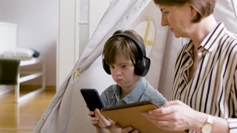 teenager with down syndrome using headphones and mobile phone, and talking with her mother, who is using tablet