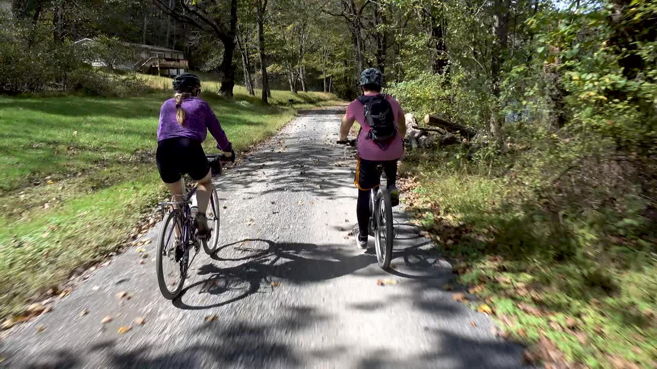 Two people cycling on a gravel road through a forest