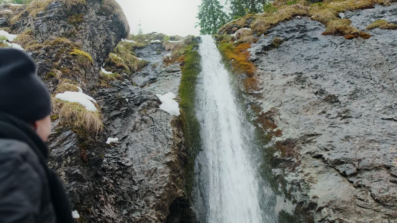 Person står foran en foss i et vinterlig fjellandskap