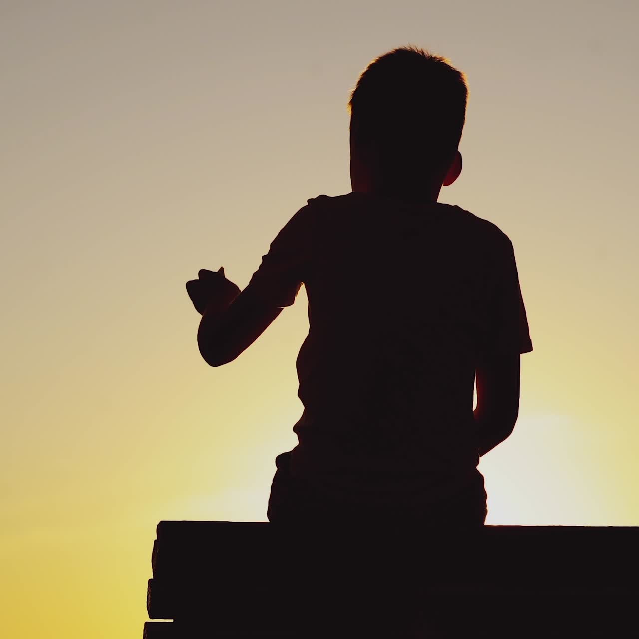 boy is holding paper ship in his hand and playing with it on the background of sunset by the river in the summer