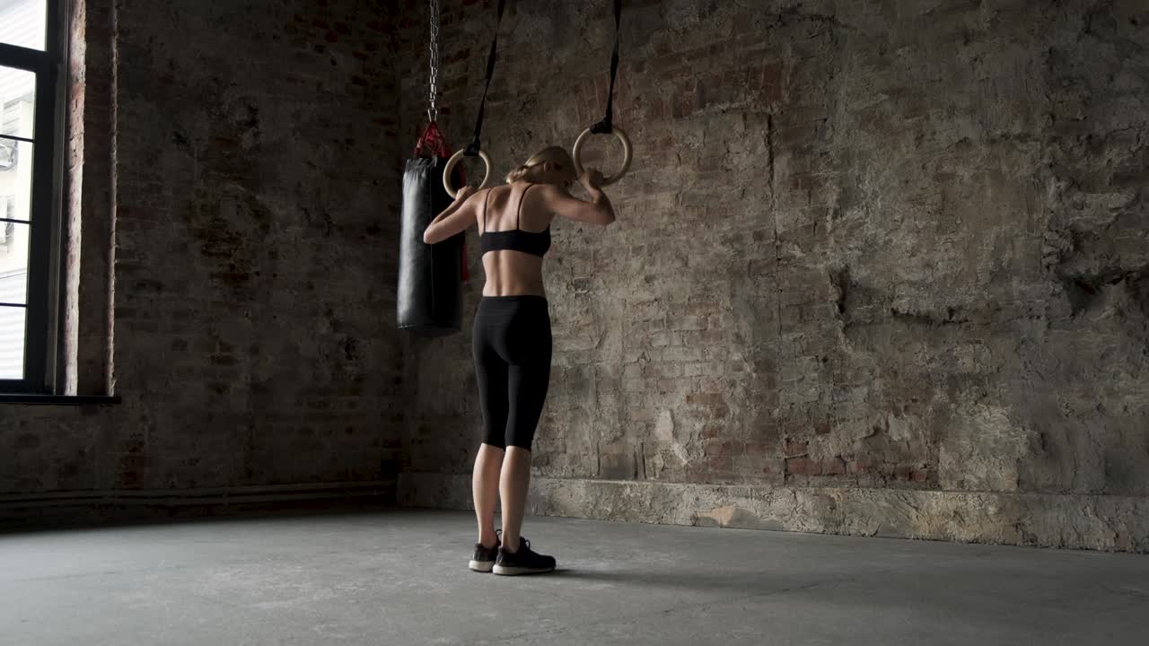 Giovane donna in forma che fa stretching agli anelli da ginnastica. Giovane atleta muscolosa che si allena con gli anelli in palestra. Giovane donna in forma che fa trazioni agli anelli da ginnastica