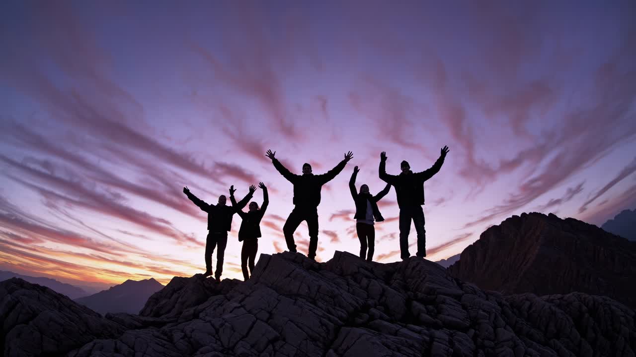 Silhouetted group atop a mountain at sunset, holding hands. Captured from a low angle, perfect