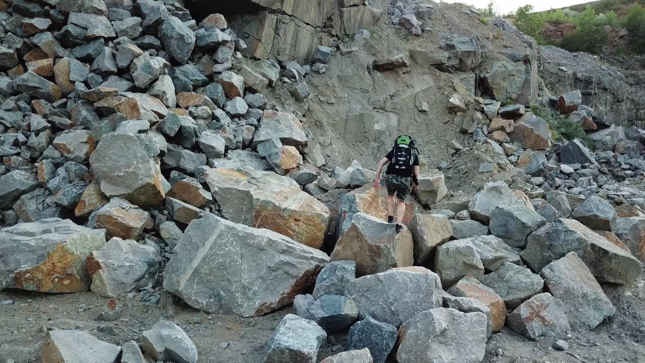 Natural background of a rocky place and a tourist climbing in summer. Hiker walking over the large pile of stones in a mountainous area.