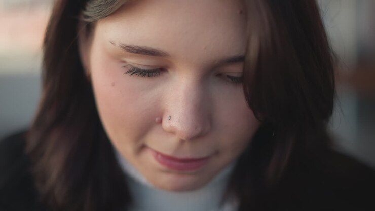 Close-up of white woman with pink lips and small nose ring, eyes closed, focused and calm expression, showing natural beauty with soft lighting and gentle features