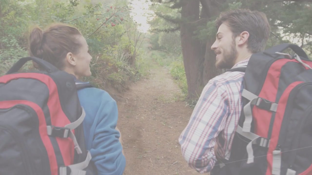 Coppia di escursionisti che entra in un sentiero stretto con zaini, camminando mentre si scambiano sorrisi, parlando per divertimento.