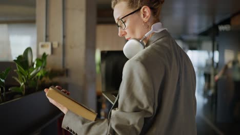 una mujer de negocios de mediana edad con gafas y un traje de negocios gris se encuentra en una oficina moderna y mira un libro