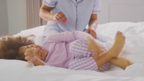 family with two mums wearing pyjamas playing on bed at home with daughter