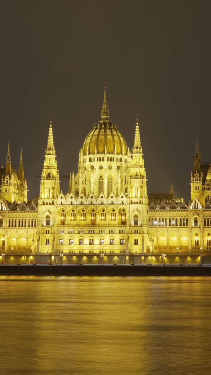 Un maestoso timelapse verticale notturno del Parlamento Ungherese illuminato a Budapest, che si riflette sul Danubio, mettendo in mostra la sua architettura iconica e l'eleganza storica.