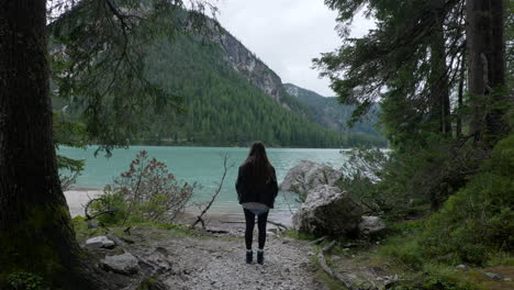 Young-adventurous-female-walking-toward-lake-and-stops-to-admire-Dolomites,-back-view