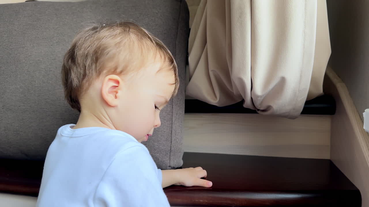 Adorable Caucasian boy sitting on the stair playing with his bare foot. Baby having good time at home near the window.