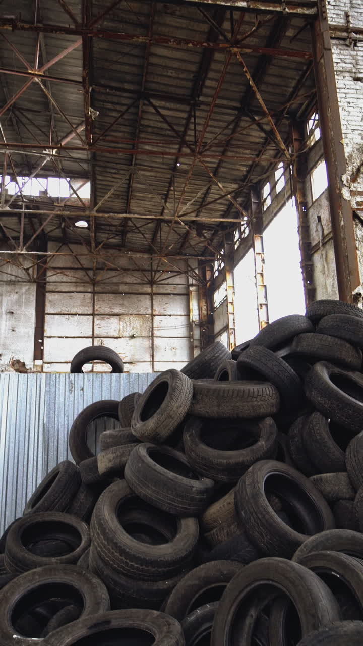 Landfill of used automobile tires on the old abandoned plant inside. Huge piles of black waste wheels from different vehicles. Motion bottom up Vertical video