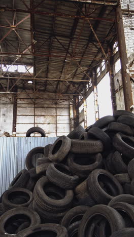 landfill of used automobile tires on the old abandoned plant inside. huge piles of black waste wheels from different vehicles. motion bottom up vertical video