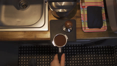 barista tamping coffee grinds at a coffee machine inside a small cafe bar