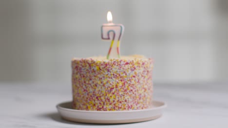 studio shot birthday cake covered with decorations and lit candle celebrating seventh birthday being blown out