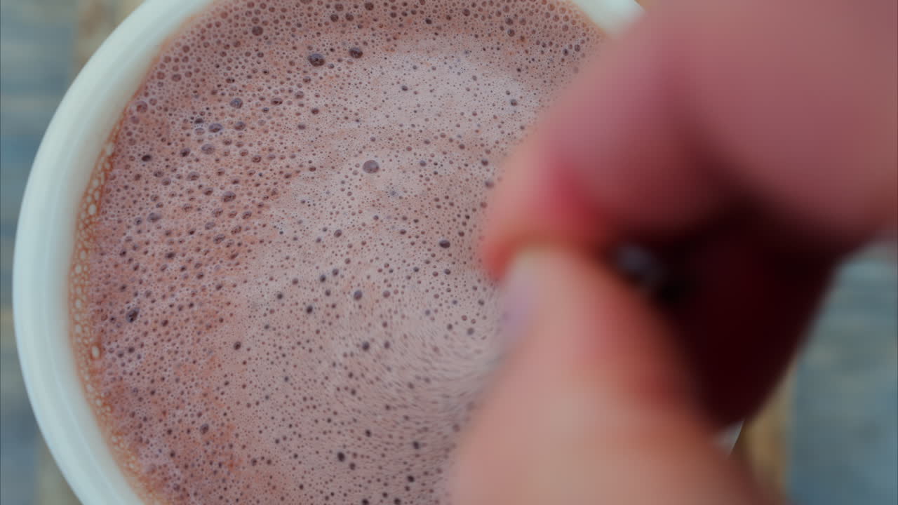Close up of a hand mixing into a a cup of hot chocolate with a spoon