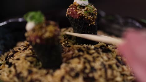 close-up of chopsticks picking sushi rolls from a bed of seasoned rice.