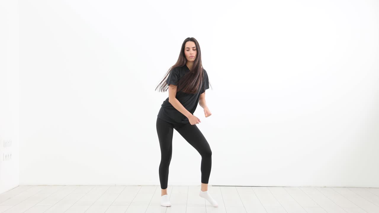 黒い服の女性がスタジオの床で腕を順に動かしながら踊る