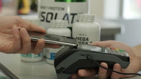 customer at counter buys sports nutrition paying with smartphone through contactless nfc bank terminal.