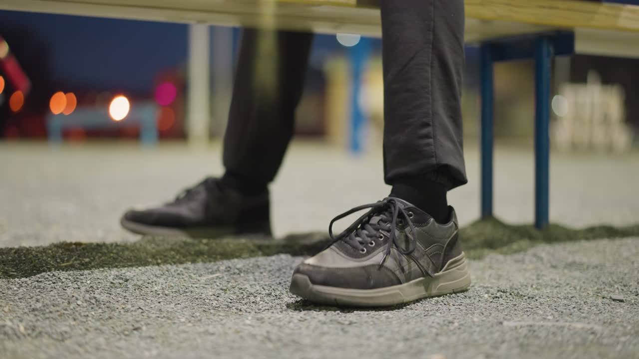 Close-up view of a person's legs, showing them tapping his foot on the ground repeatedly, the background is dimly lit and blurred