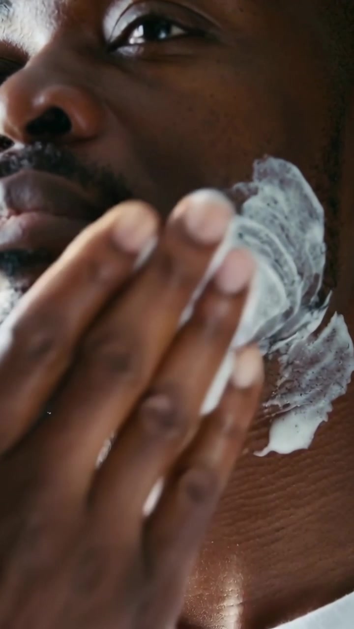 Vídeo vertical: Mão levantando, homem de camisa branca aplicando espuma com esfoliante na penteadeira para se cuidar
