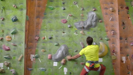 climber getting geared up with harness lead rope chalk bag carabiner and belay. man climber climbs the wall with a rope to the top