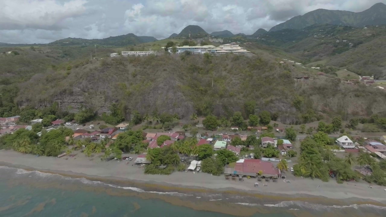 Il drone si allontana dall'ospedale nord Caraibe verso il bordo della spiaggia del coin in Martinica, Francia, con il vulcano Pelée sullo sfondo