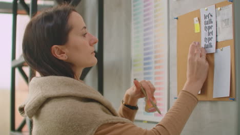 una mujer diseñadora de pie en la pared adjunta sus ideas a la selección de colores de la pared y la colorística. eligiendo un color y preparándose para crear una solución de diseño y color.