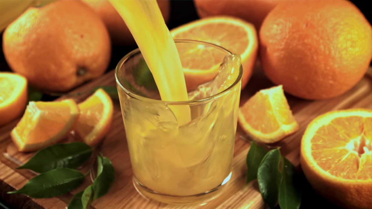 Fresh Orange Juice Poured into a Glass with Oranges on a Wooden Board