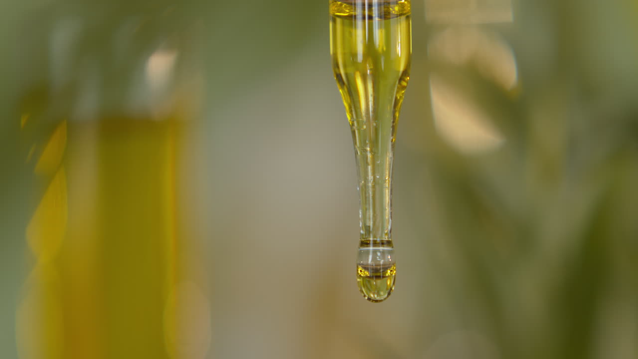 капля желтой жидкости, падающая из стеклянной пипетки, крупный план