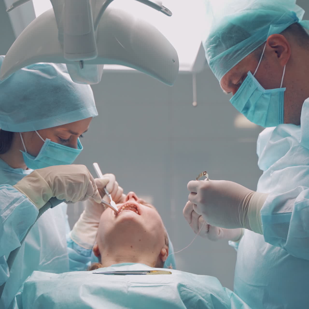 Dentist male works with a thread in patient's mouth in dental clinic. Specialist man and his assistant in medical uniform treat female's teeth in the stomatology center. Dental operation.
