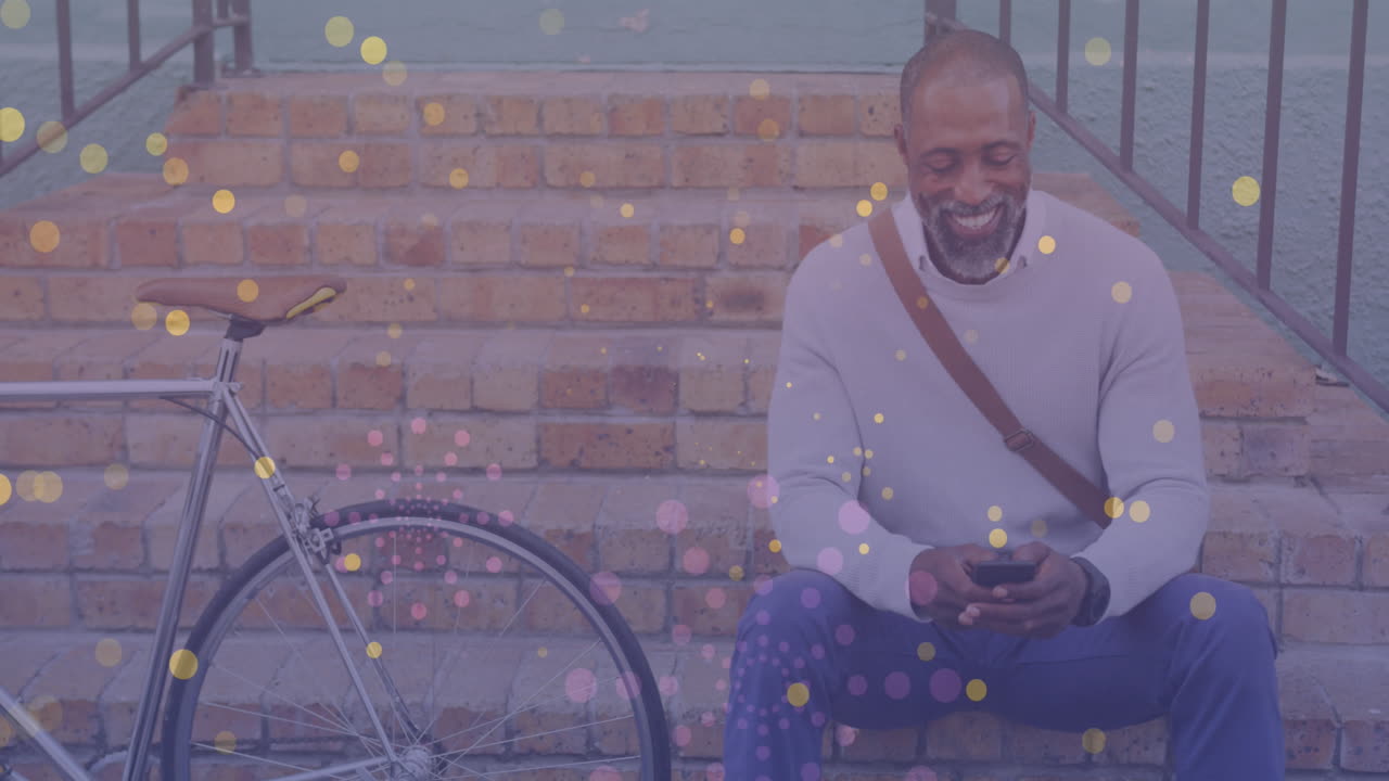 Yellow spots of light floating against african american man with a bicycle using smartphone