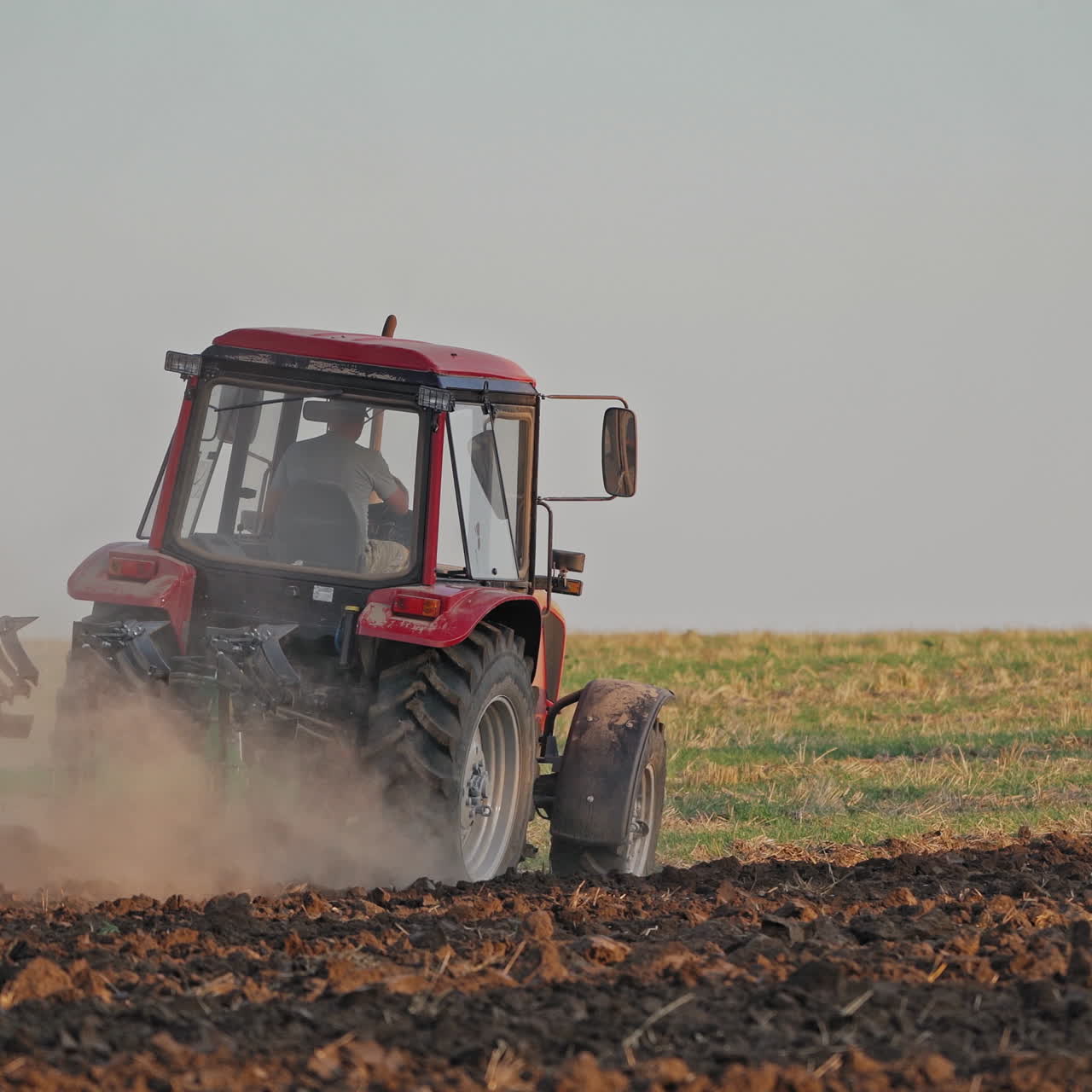 Back view of a tractor plowing the soil. Agricultural machinery preparing land for further works on the field. Process of cultivation the ground.