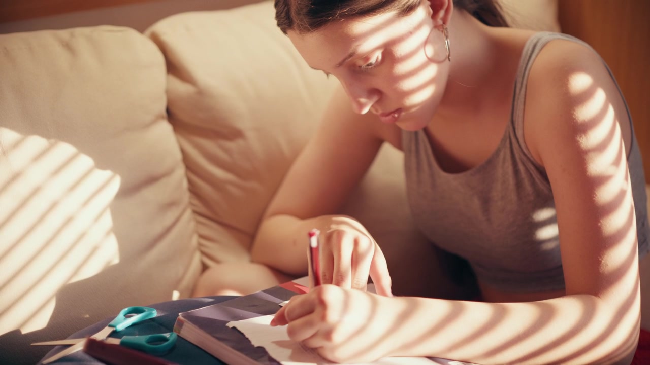 Close-up de uma estudante do ensino médio focada criando anotações secretas e cábulas a partir do seu smartphone para colar numa prova futura, usando tesoura e fita adesiva em um sofá.