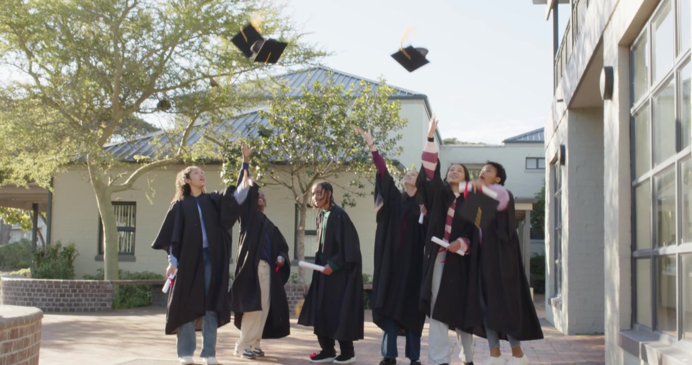 Laureati di diverse etnie in toga nera che sistemano i cappelli, tengono i diplomi, festeggiano lanciando i cappelli in piazza