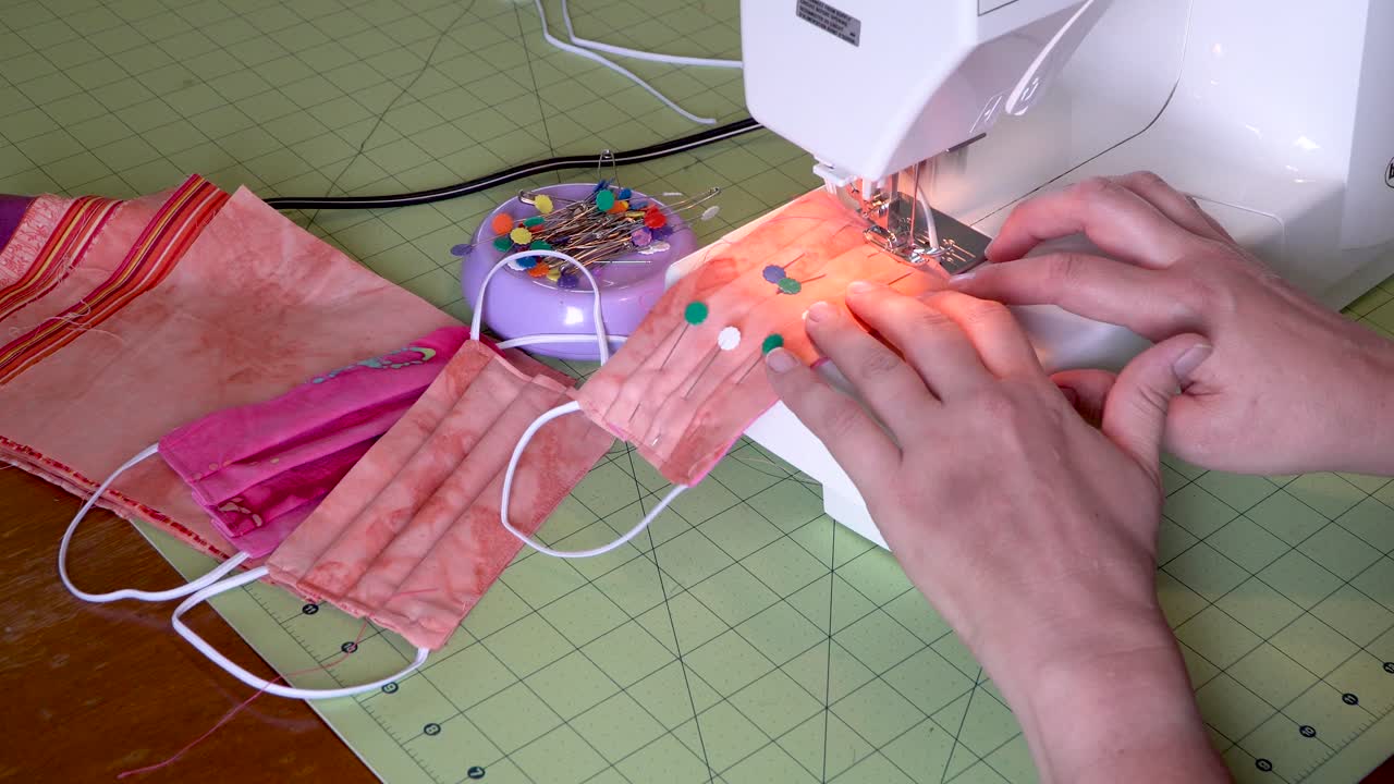 여자는 바이러스 노출 예방을 위해 보호 직물 안면 마스크를 꿰맨다