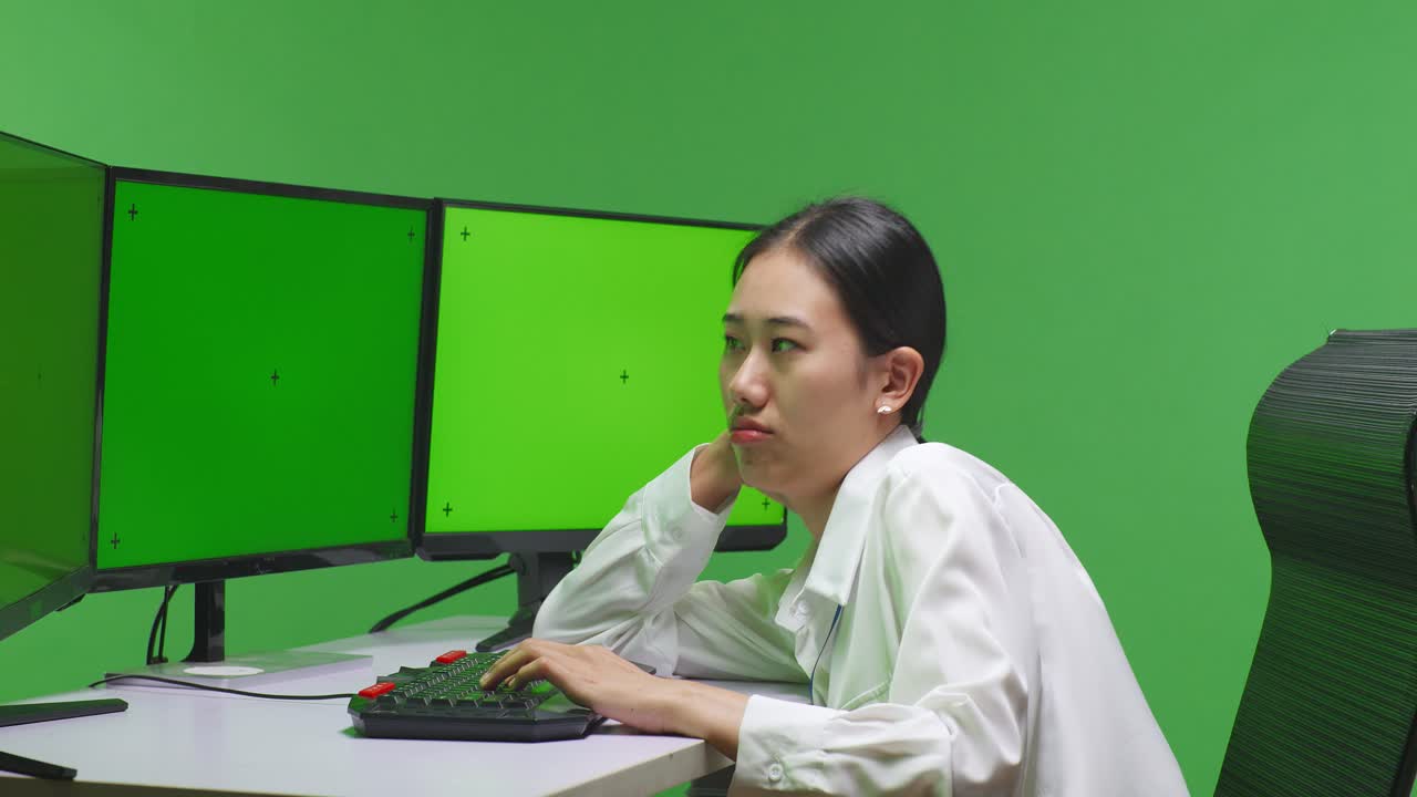 여러 개의 녹색 화면을 가진 컴퓨터에서 일하는 여성