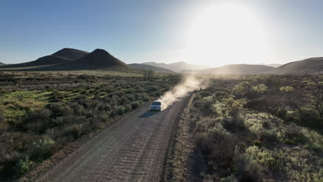 Aerial-shot-of-car-driving-on-dirt-road-in-Willcox,-Arizona,-drone-shot-with-mountains-in-the-background-and-dust-behind-the-car