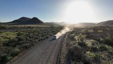 toma aérea de un coche conduciendo por un camino de tierra en willcox, arizona, toma de un dron con montañas en el fondo y polvo detrás del coche