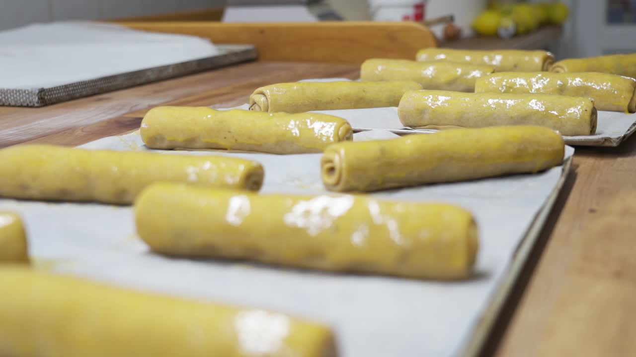 varios troncos de masa de bejgli lavados con huevos colocados cuidadosamente en bandejas de horneado listos para el horno