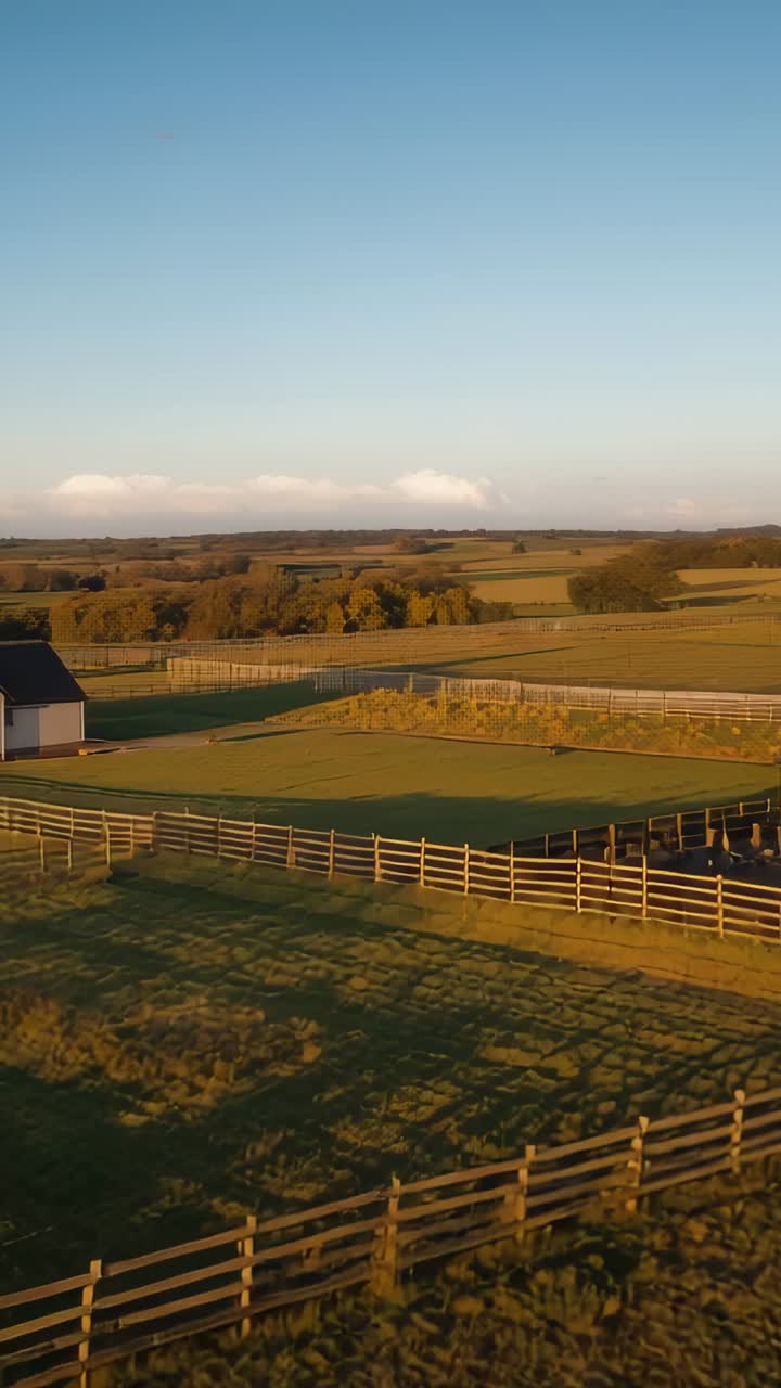 Vertical video: Panning camera over farm fences at sunrise, revealing outbuilding and barn