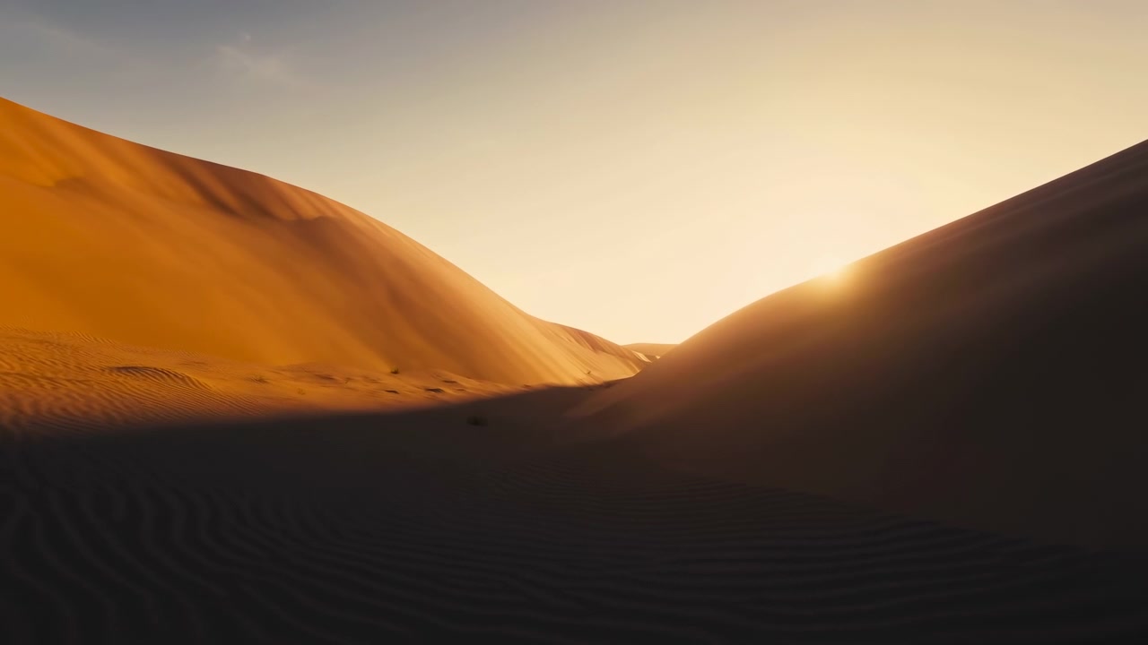 Vista dal basso all'interno di una valle desertica a forma di V che mostra il sole che sorge sulla cresta di una duna mentre la luce calda si diffonde sui pendii di sabbia e il primo piano rimane in ombra fresca, creando un tranquillo contrasto scenico.