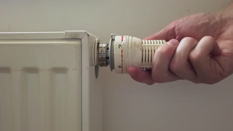 disparo lateral estático de una mano masculina girando la válvula del radiador termostático a cero
