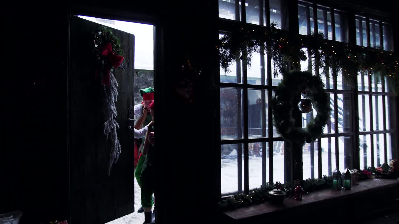 Santa and elves in decorated room. Santa's residence and two elves in fairy suits comes inside. Christmas atmosphere