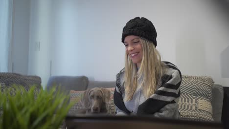 A-joyful-woman-doing-a-video-call-while-sitting-with-her-dog-and-drinking-coffee