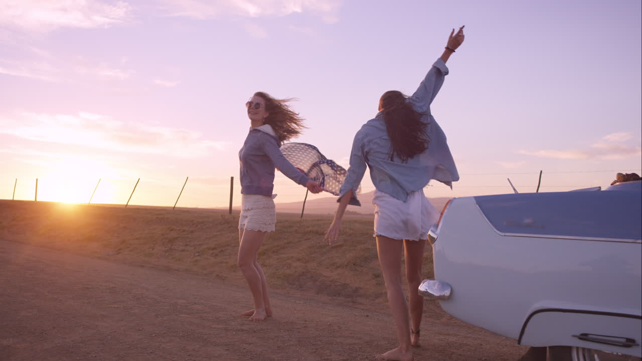 amigas bailando al atardecer en un viaje por carretera con un coche antiguo