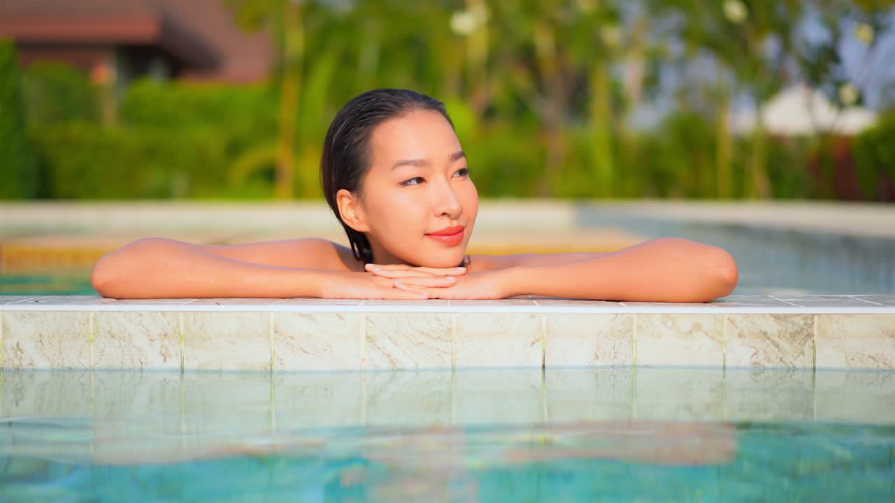 수영장 가장자리를 따라 팔에 머리를 얹고 있는 예쁜 젊은 여성의 클로즈업이 머리를 들고 눈을 뜬다
