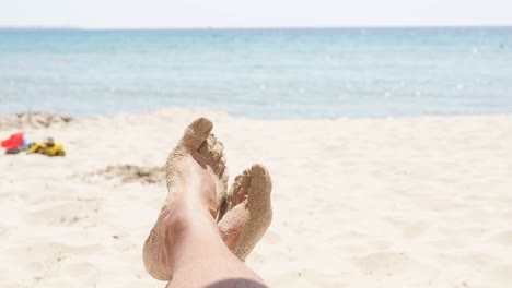 close-up of men's feet on a sandy beach against a background of azure sea and blue sky