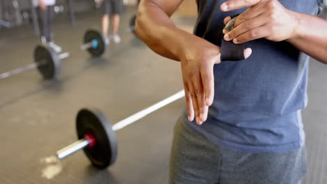 sección media de un hombre biracial atando los dedos antes del entrenamiento con pesas en el gimnasio, en cámara lenta