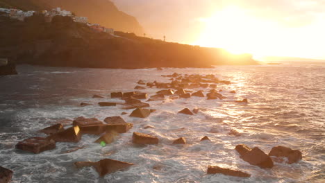 Side view Steep volcanic shore at sunset, reefs of volcanic lava, stormy ocean, white foam from the giant waves that hit rocks. Aerial shot. Garachico, Tenerife, Canary Islands.